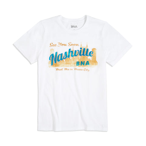 Full shot of the BNA Postcard Women's Tee.  Light tan and teal design looks like a vintage postcard with "See You Soon" in a script font printed above an illustration of the Nashville Skyline.  "Nashville" is superimposed over the skyline, with the tag line "Meet me in Music City" below.