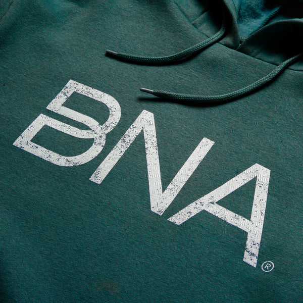Detail shot of dark green hoodie sweatshirt with white distressed BNA logo centered on the chest.  BNA logo features a unique infinity "B."