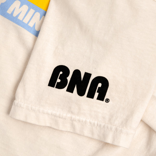 Detailed view of cream t-shirt with BNA in retro bubble font on left sleeve.