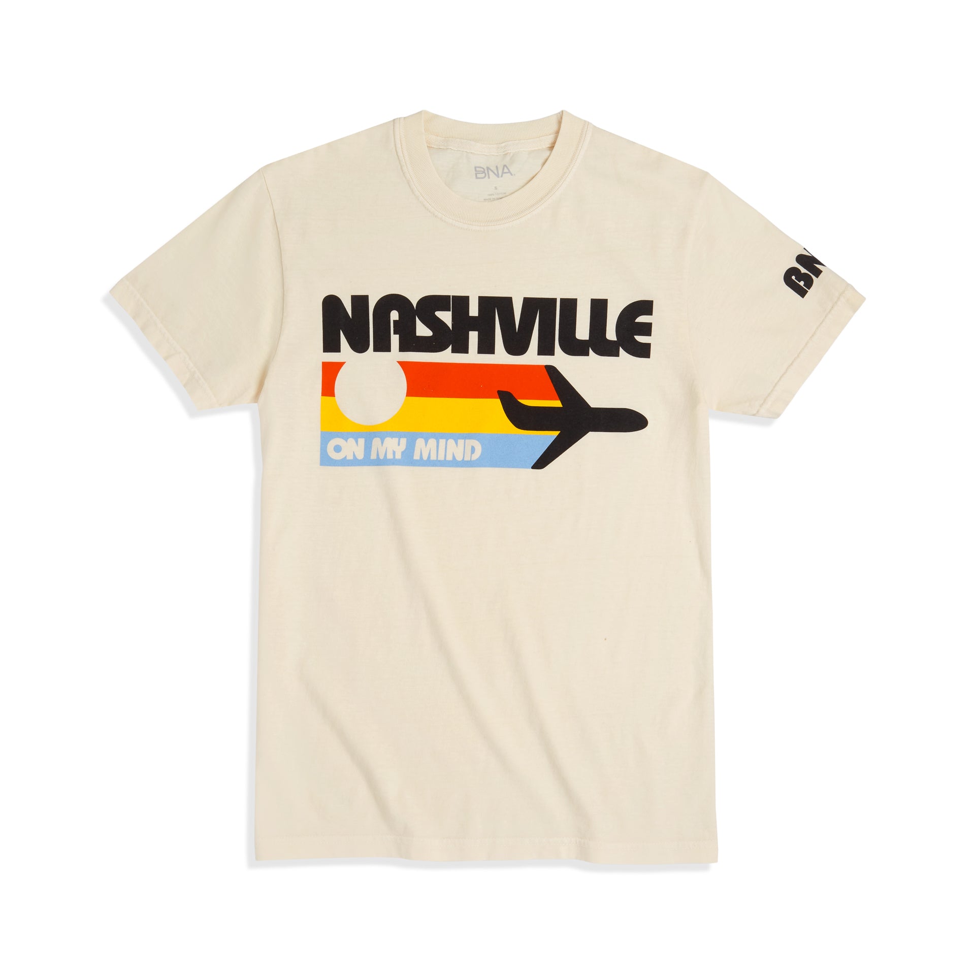 Cream t-shirt with large chest graphic depicting a black plane and three vintage stripes in orange, yellow, and light blue.  Tee reads "Nashville on my mind" in retro bubble letters and BNA on the sleeve.