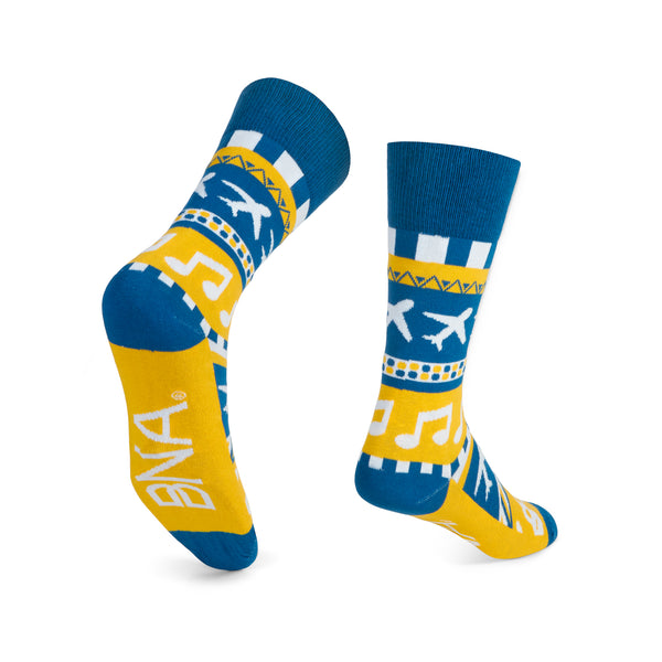 Back view of patterned socks made to look like a sweater that feature music notes, guitars, planes, and geometric stripes in our signature color palette of blue, gold, and white.  Cuff, heel, and toe are BNA blue.  BNA logo on base of foot.