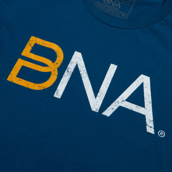 Detail shot of blue crewneck t-shirt with yellow and white distressed BNA logo centered on the chest.  BNA logo features a unique infinity "B."
