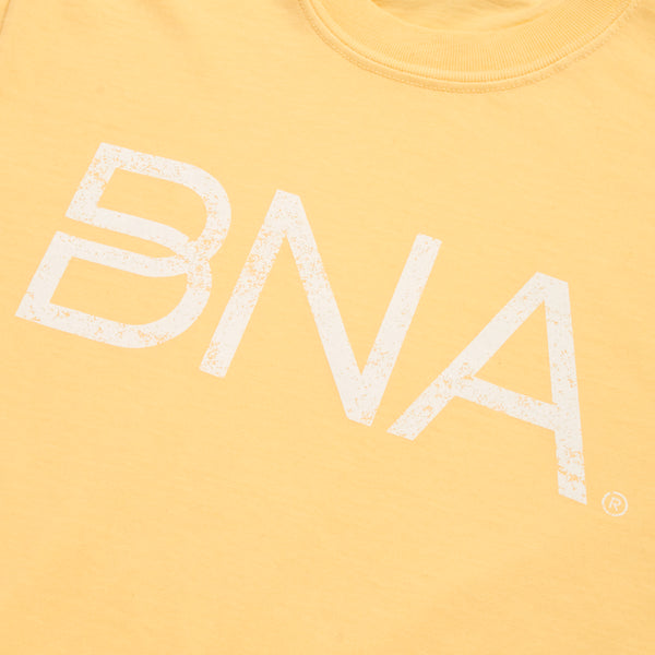 Close-up of yellow crewneck t-shirt with white distressed BNA logo centered on the chest.  BNA logo features a unique infinity "B."