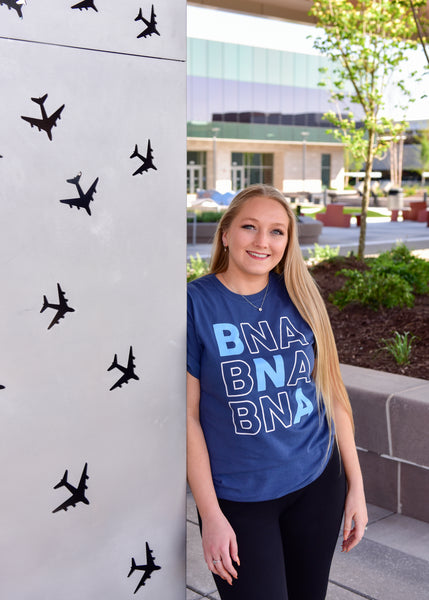 A female model wears the short sleeve BNA Wordplay Tee outdoors at BNA.