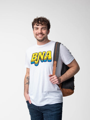 Man wearing BNA Groove T-shirt.  T-shirt is white with BNA in large, retro-style bubble letters. Letters are yellow, with a black outline and subsequent drop shadow in orange, aqua, and royal blue.  