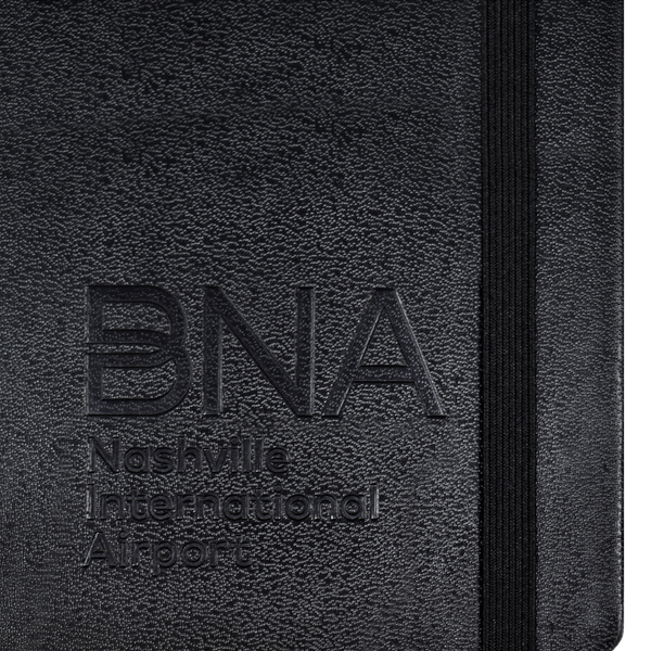 Detail shot of embossed BNA logo on cover of black Moleskine notebook.
