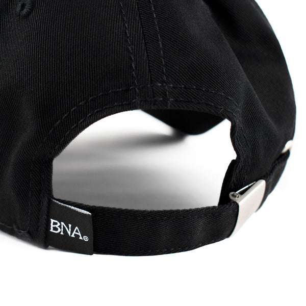 Back detail of hat with metal closure and woven tag in black with BNA in white lettering.