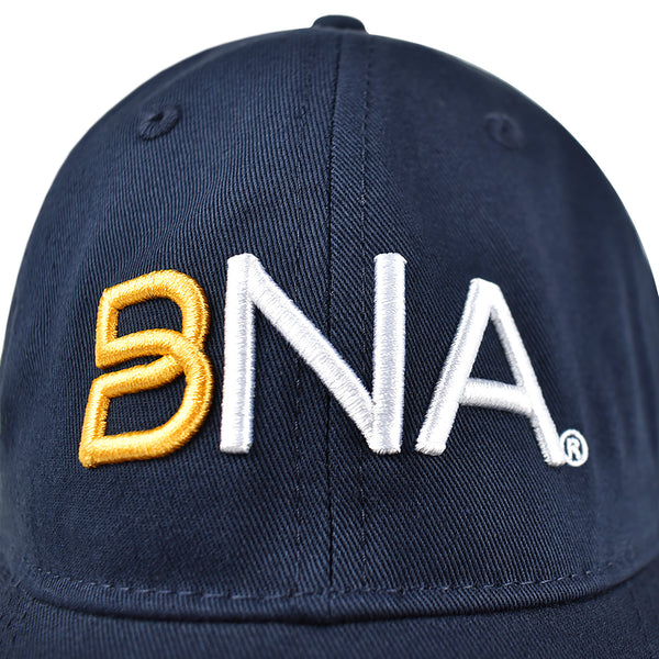 Detail shot of front of hat.  Navy blue ballcap with BNA logo in 3d embroidery.  B is gold and NA is white.