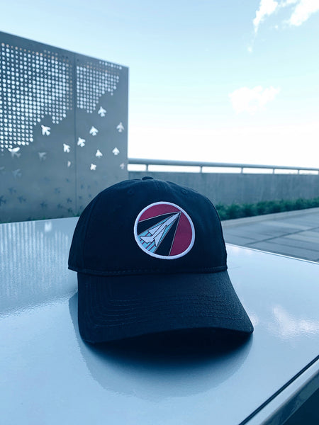 A view of the black Throwback Dad Cap featuring retro BNA logo patch on front.  Cap is sitting on a silver table with a sky and outdoor setting behind it.